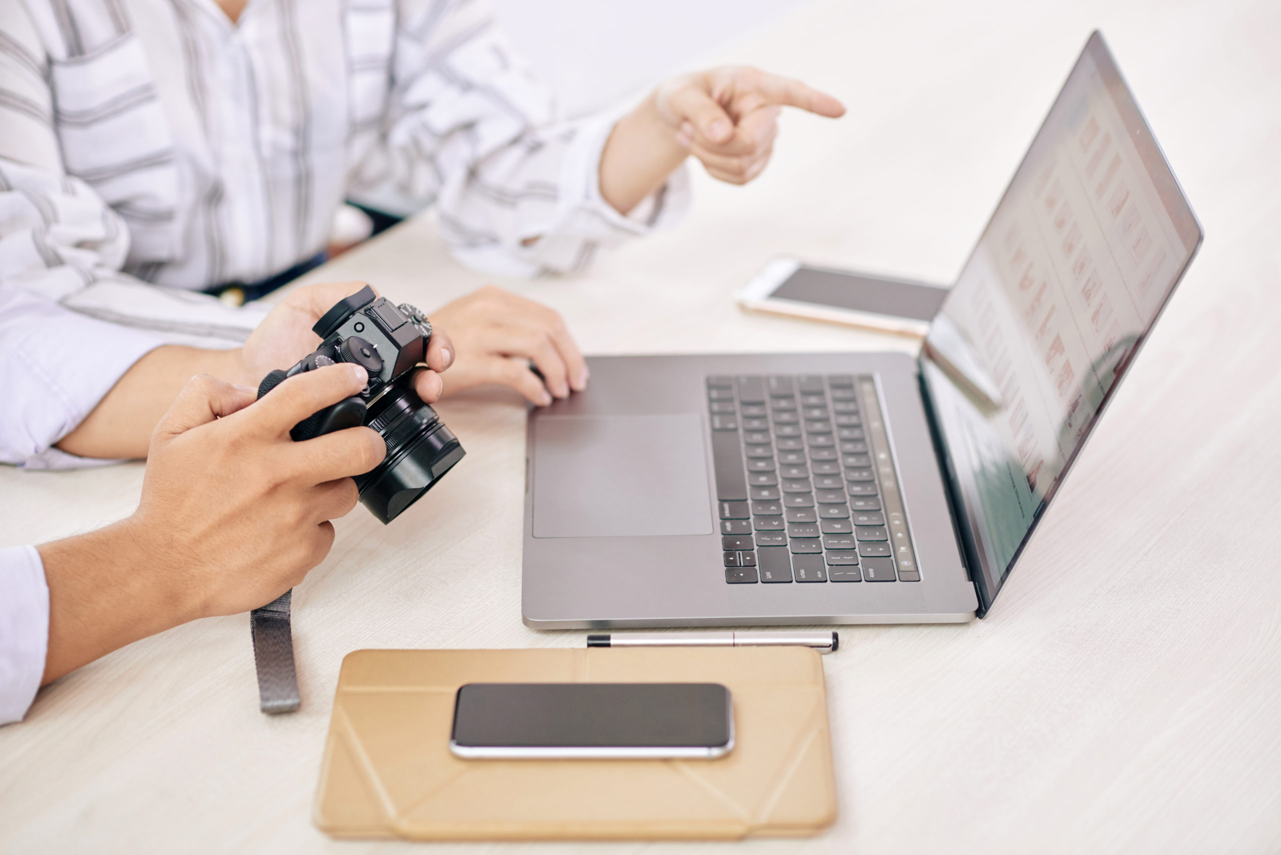 Crop shot of modern photographers with photo camera using laptop at table in office